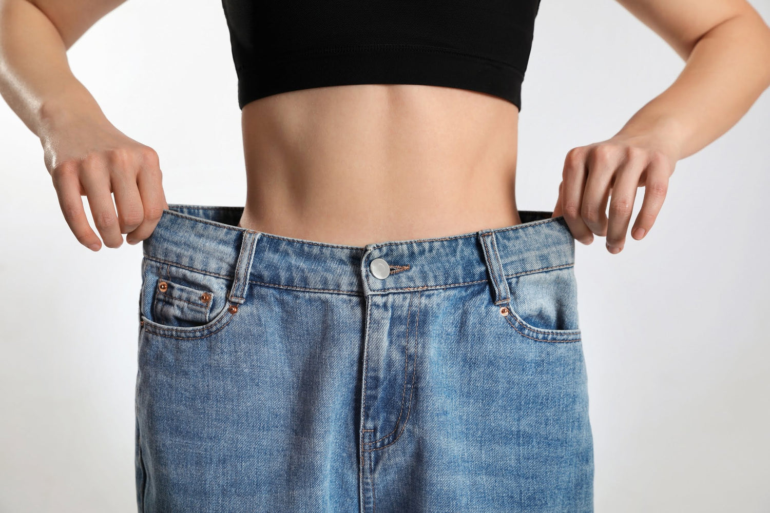 Woman showing how much weight she lost with Wegovy by holding out the waistband of her old jeans – visual proof of slimming and reduced waist size