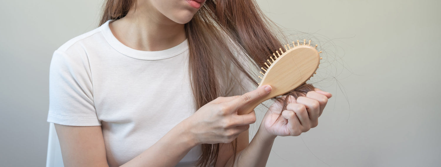 Young woman brushing her hair and noticing excessive hair strands on the brush, with a concerned expression, symbolizing hair thinning and the need for targeted hair restoration treatment.