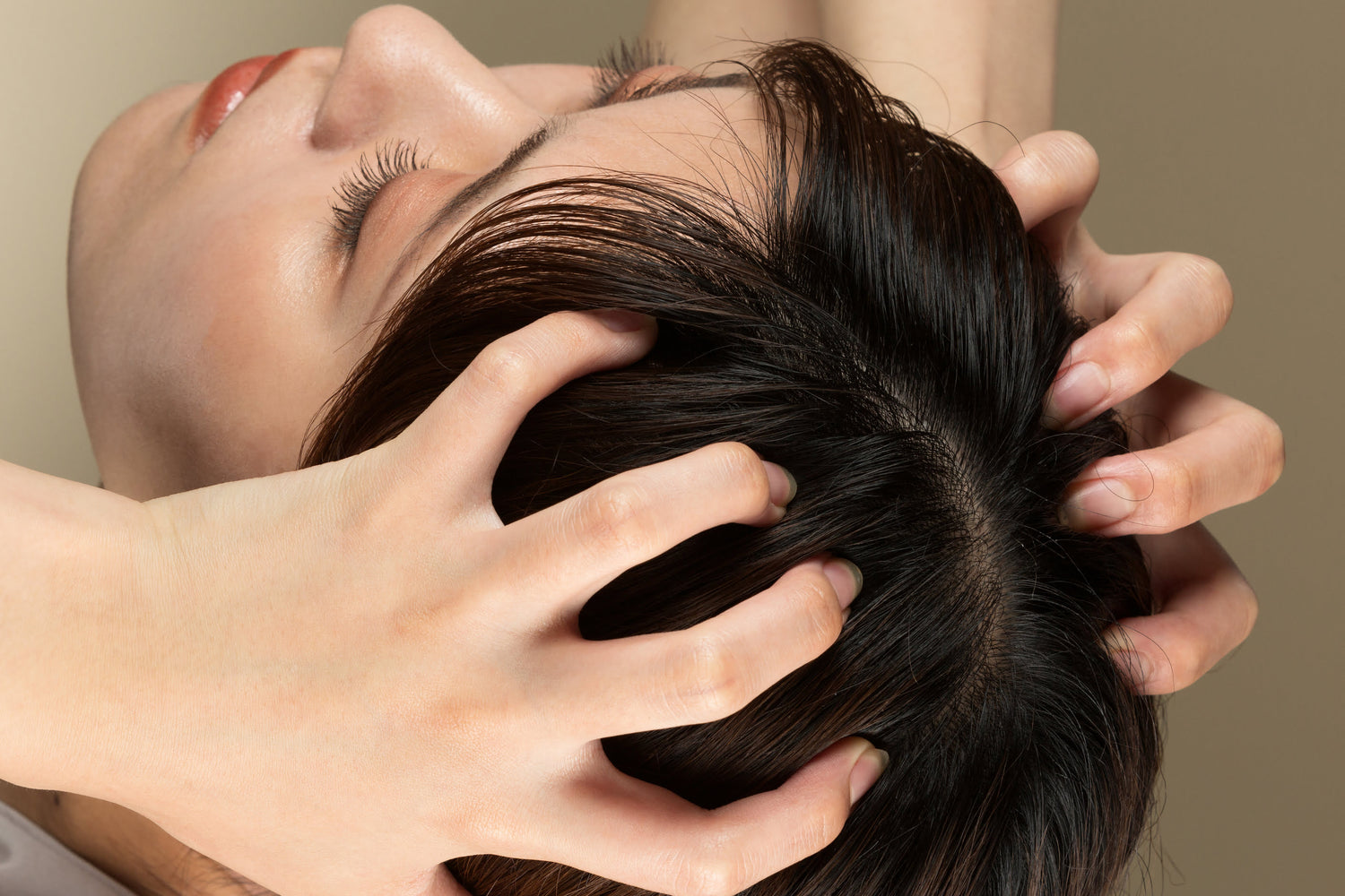 Smiling woman running fingers through thick, shiny, and healthy hair, demonstrating visible scalp and hair improvements after HydraFacial Keravive treatment